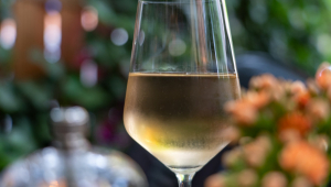 Vinho branco servido até a metade em uma taça. Cenário em volta está desfocado